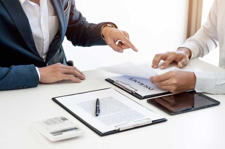 A middle-aged couple reading through insurance documents at their kitchen table.